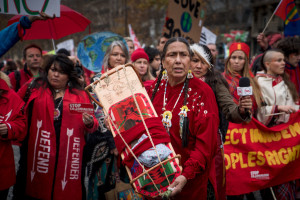 asey Camp-Horinek of the Ponca Nation, Oklahoma presents a traditional cradleboard to the people of Paris during a march Dec. 12. The cradleboard represents future generations.. -IIndigenous Environmental Network photo